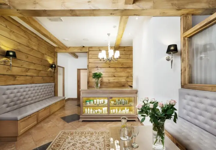 Wnętrze spa z drewnianymi elementami, kanapami, ladą z kosmetykami i bukietem róż.